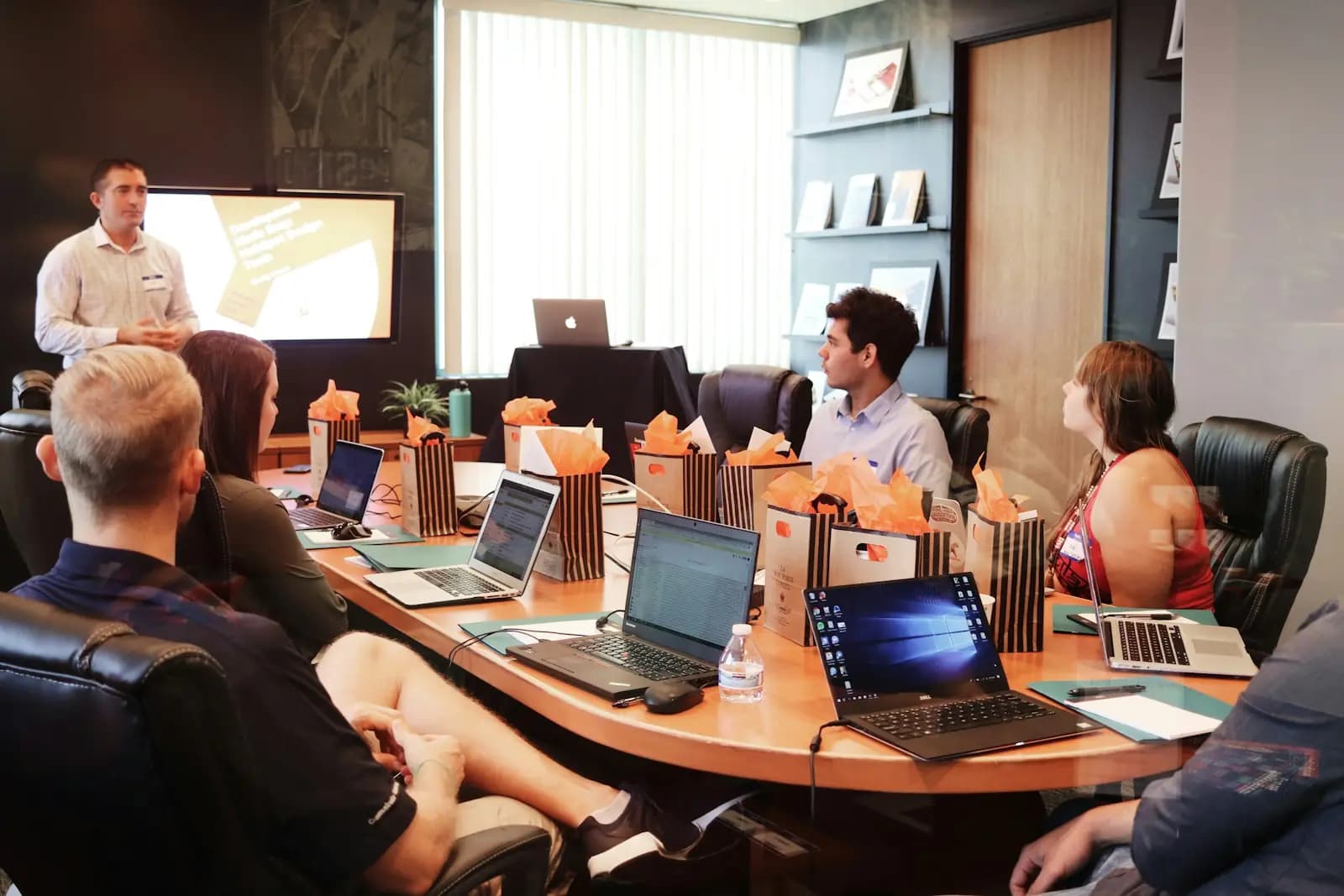 Ein Workshop: eine Person präsentiert, das Team sitzt mit Laptops am langen Tisch