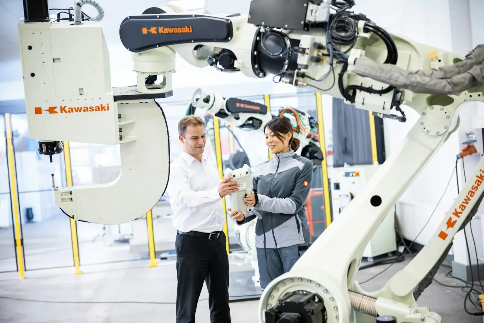 Zwei Menschen besprechen sich in einer Fertigungshalle zwischen Industrierobotern