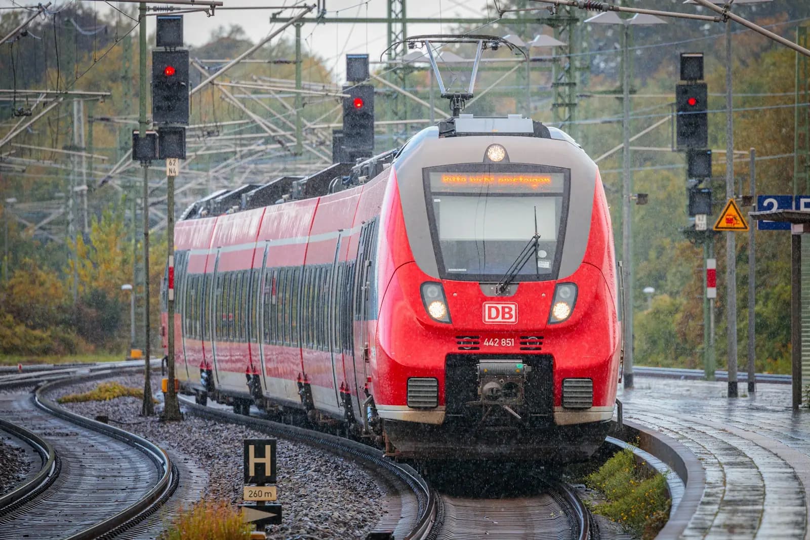 Ein roter Regionalzug fährt an Signalen vorbei durch eine gebogene Gleisanlage