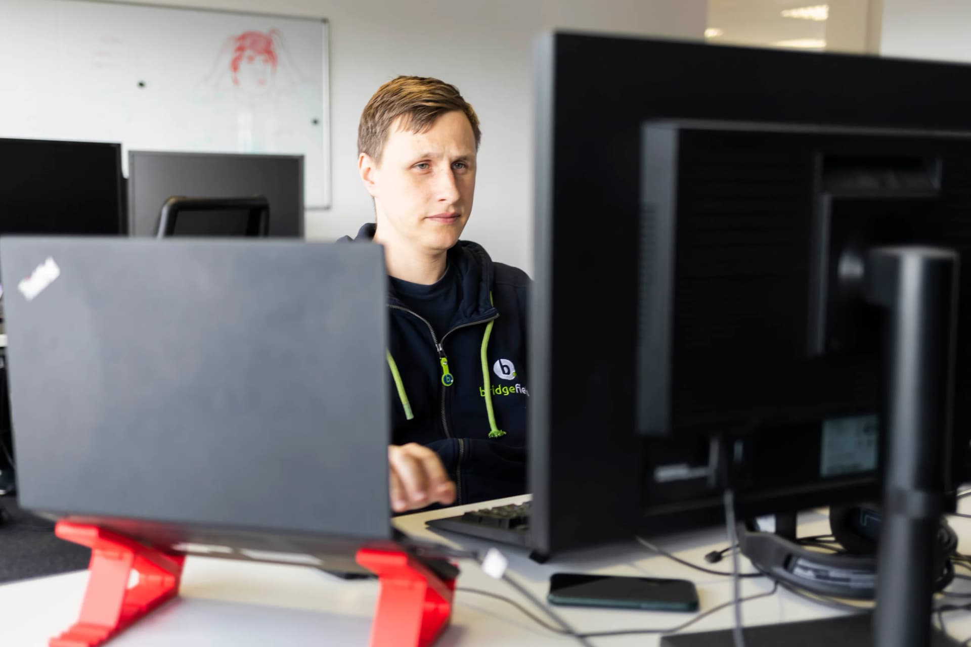 Ein Entwickler im bridgefield-Pullover arbeitet zwischen Laptop und Monitor