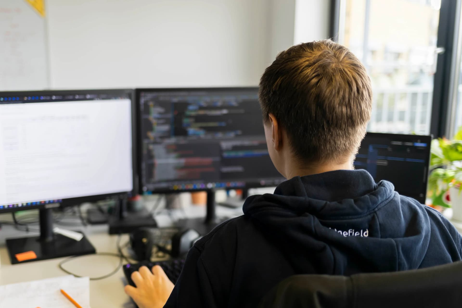 Ein Entwickler von hinten vor zwei Monitoren mit Code