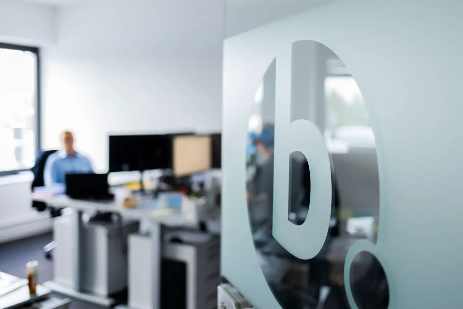 Das bridgefield-Logo auf einer gläsernen Bürowand vor Arbeitsplätzen