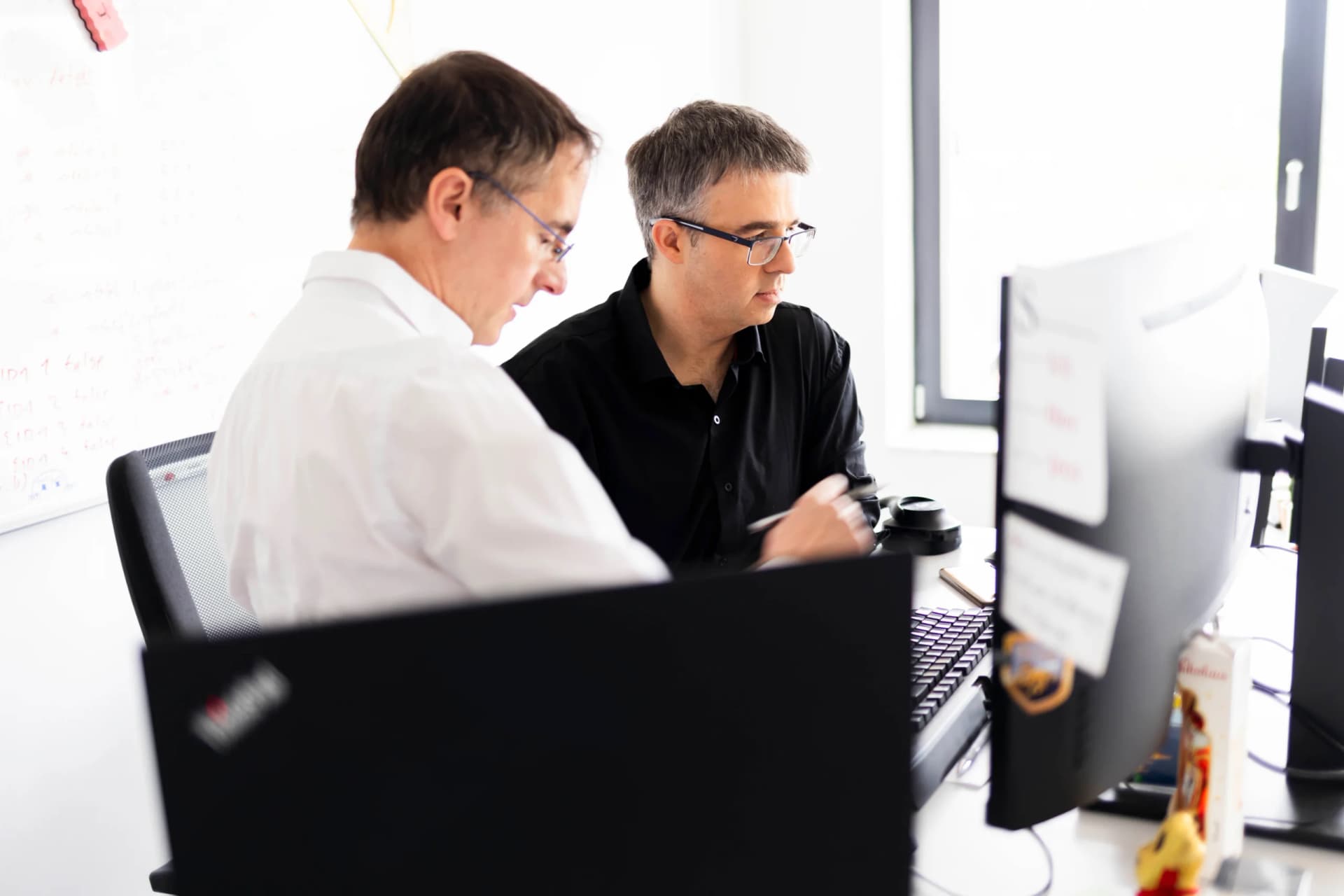Zwei Kollegen schauen gemeinsam auf einen Bildschirm und besprechen die Arbeit